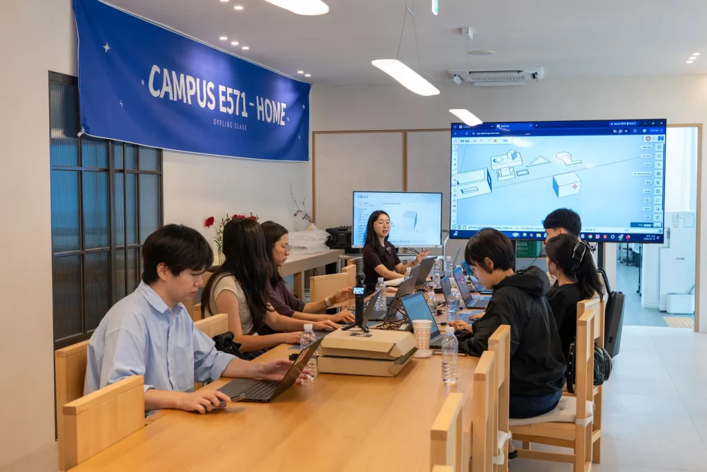 CAMPUS E571 – HOME 현수막 아래, 스크린에 띄운 3D 모델을 보며 노트북으로 따라가는 참가자들.